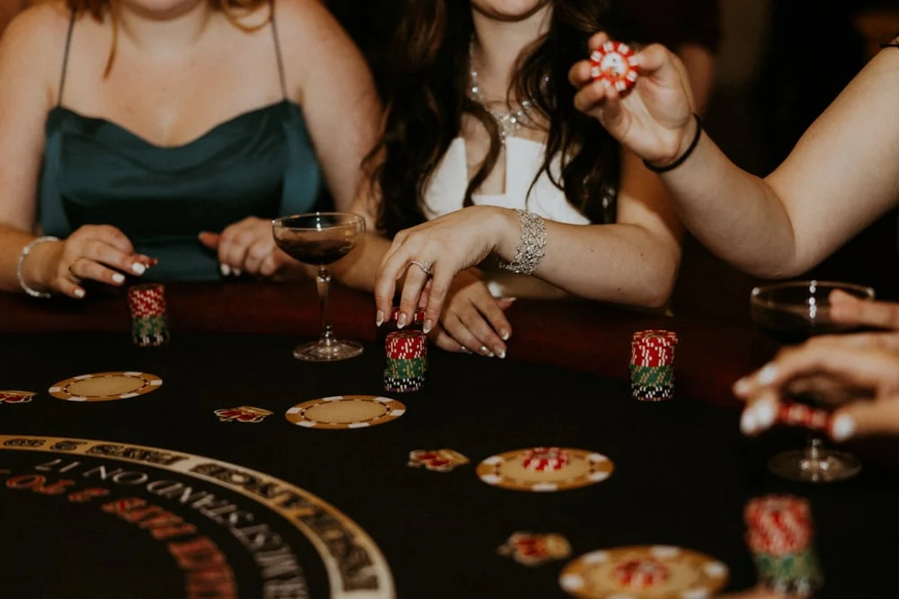 Guests playing a casino card game at a dark felt table with chips