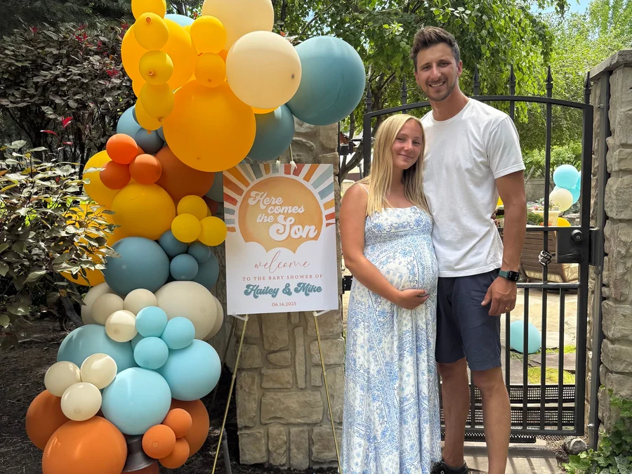Expecting couple posing beside a colorful balloon arch and welcome sign