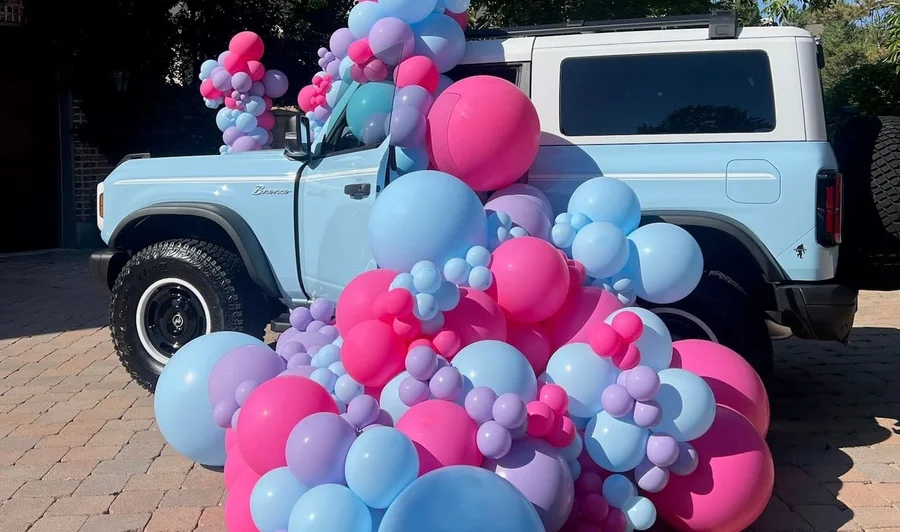 Pastel pink and blue balloon sculpture beside a light blue vintage SUV
