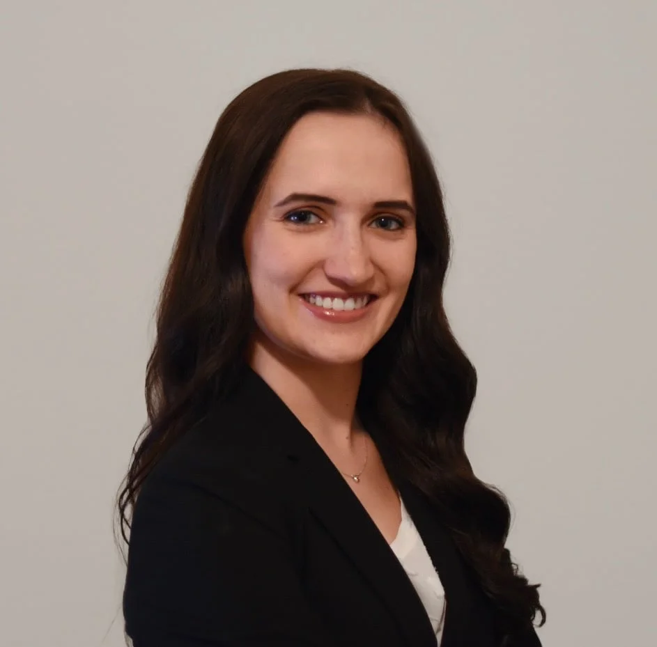 Portrait of Brooke Peña-Diamond, with long dark wavy hair, smiling in a black blazer.