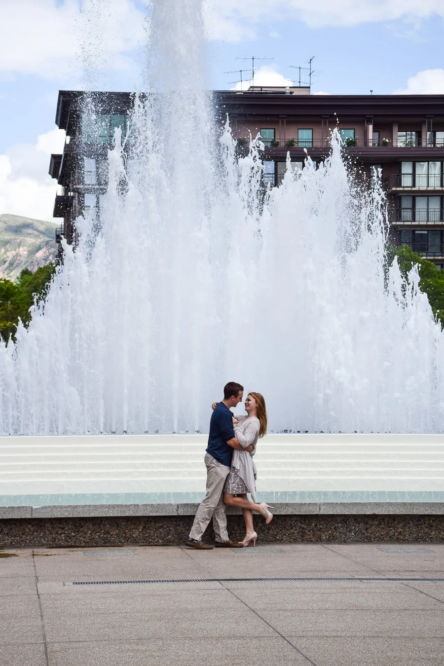 Couple embracing in front of a tall city fountain during an engagement session
