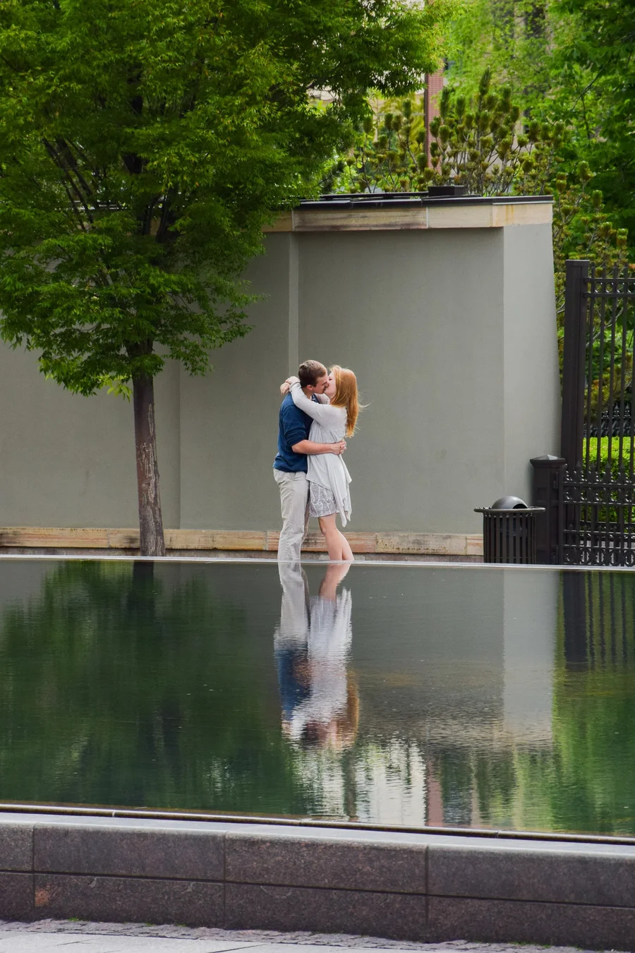 Couple kissing beside a reflecting pool in a quiet green courtyard