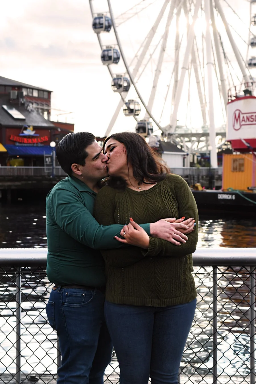 Couple kissing in front of a waterfront Ferris wheel at dusk
