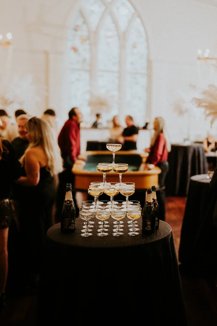 Wedding guests gathered around a champagne tower in a softly lit chapel-style reception hall.