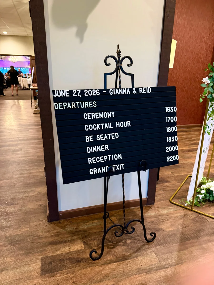 Black wedding day schedule board on an iron easel in a venue hallway