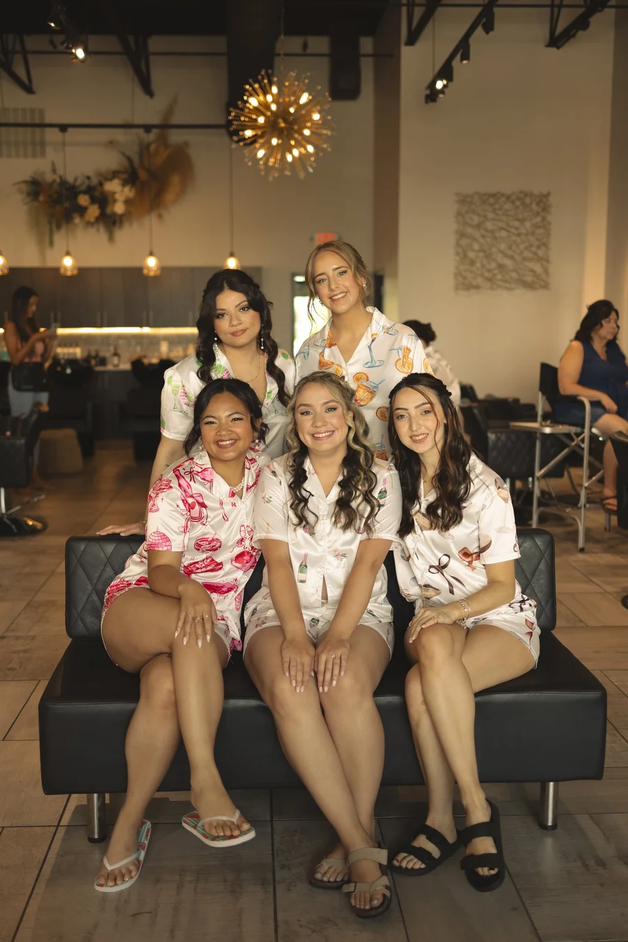 Bridesmaids in matching floral robes sitting together on a black leather sofa