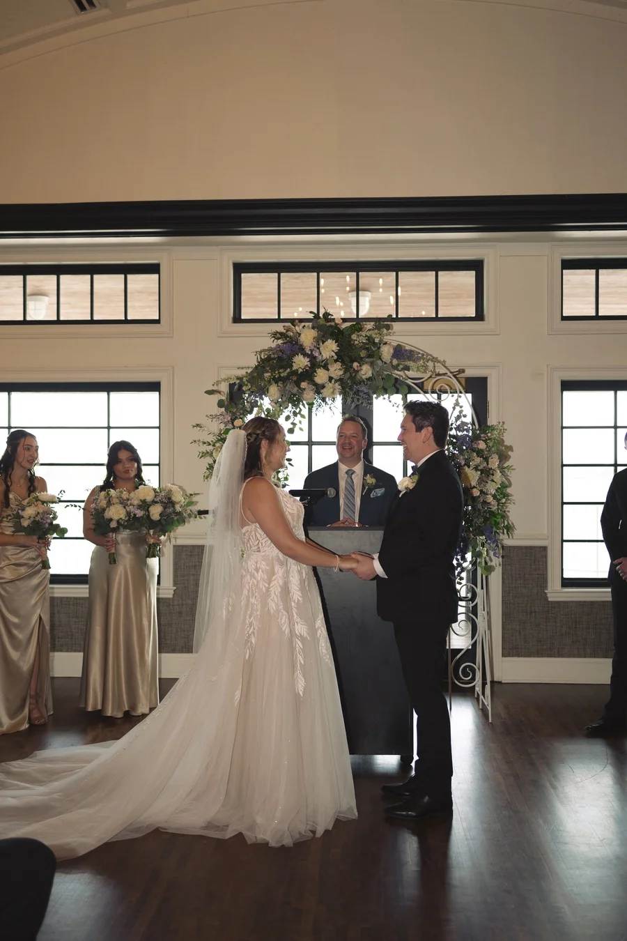 Couple exchanging vows at a floral arch with bridesmaids looking on