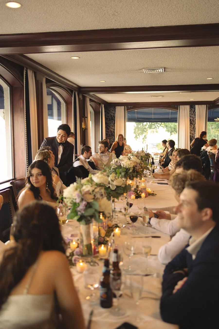 Long reception table with candles, flowers and seated guests in a lakeside dining room