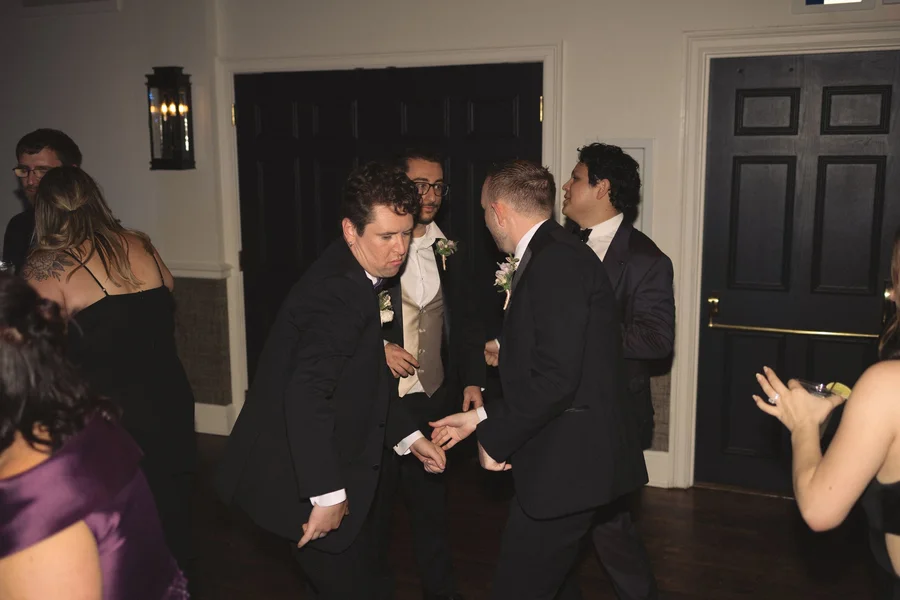 Guests dancing and cheering in a dim reception room with a groom in the circle