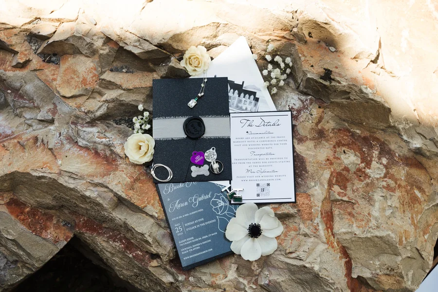 Wedding invitation and flower on a rock ledge with black stationery pieces