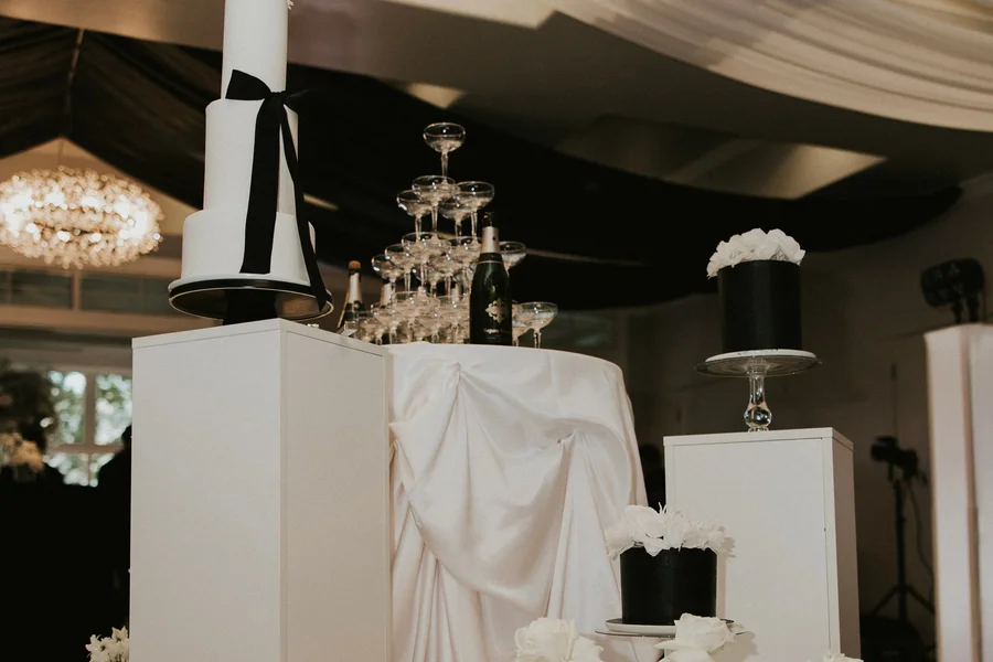Black and white reception display with a champagne tower and draped pedestals
