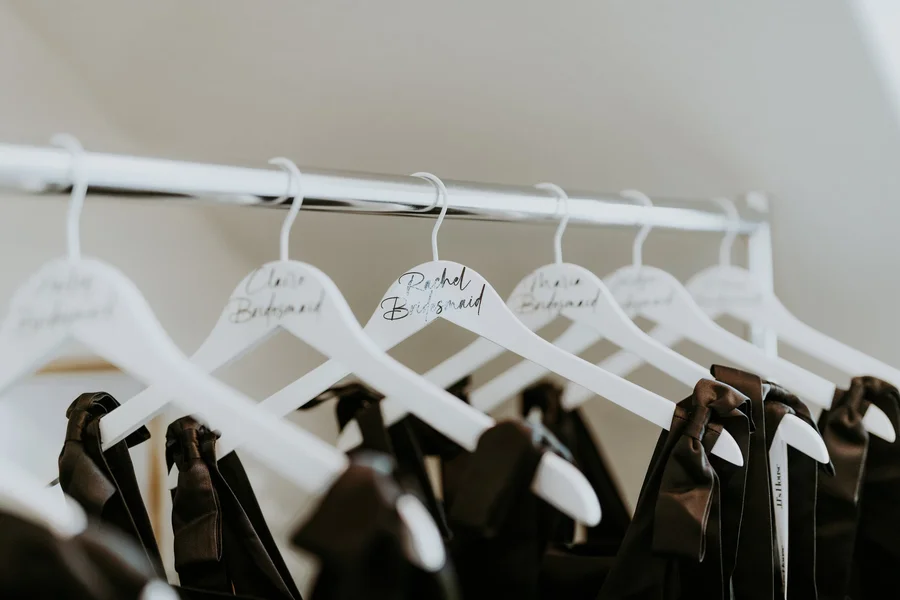 White hangers with bridal party names holding black jackets on a rail