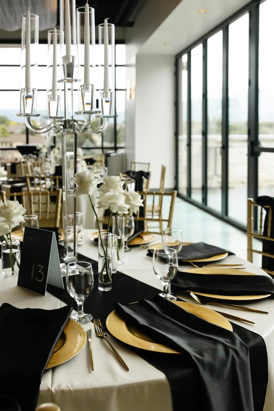 Tall candelabra centerpiece on a black and gold table by large windows