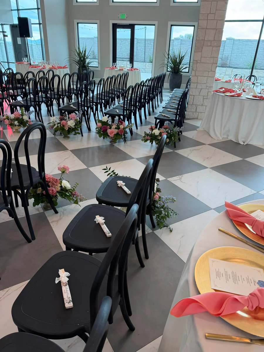 Black chairs on a checkerboard floor in a ceremony space with tables set behind