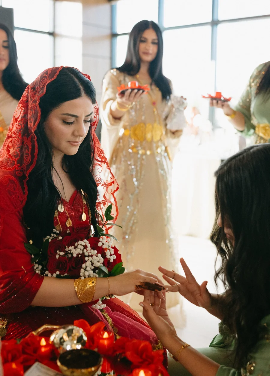 Bride in red veil having henna applied during a traditional pre-wedding ceremony