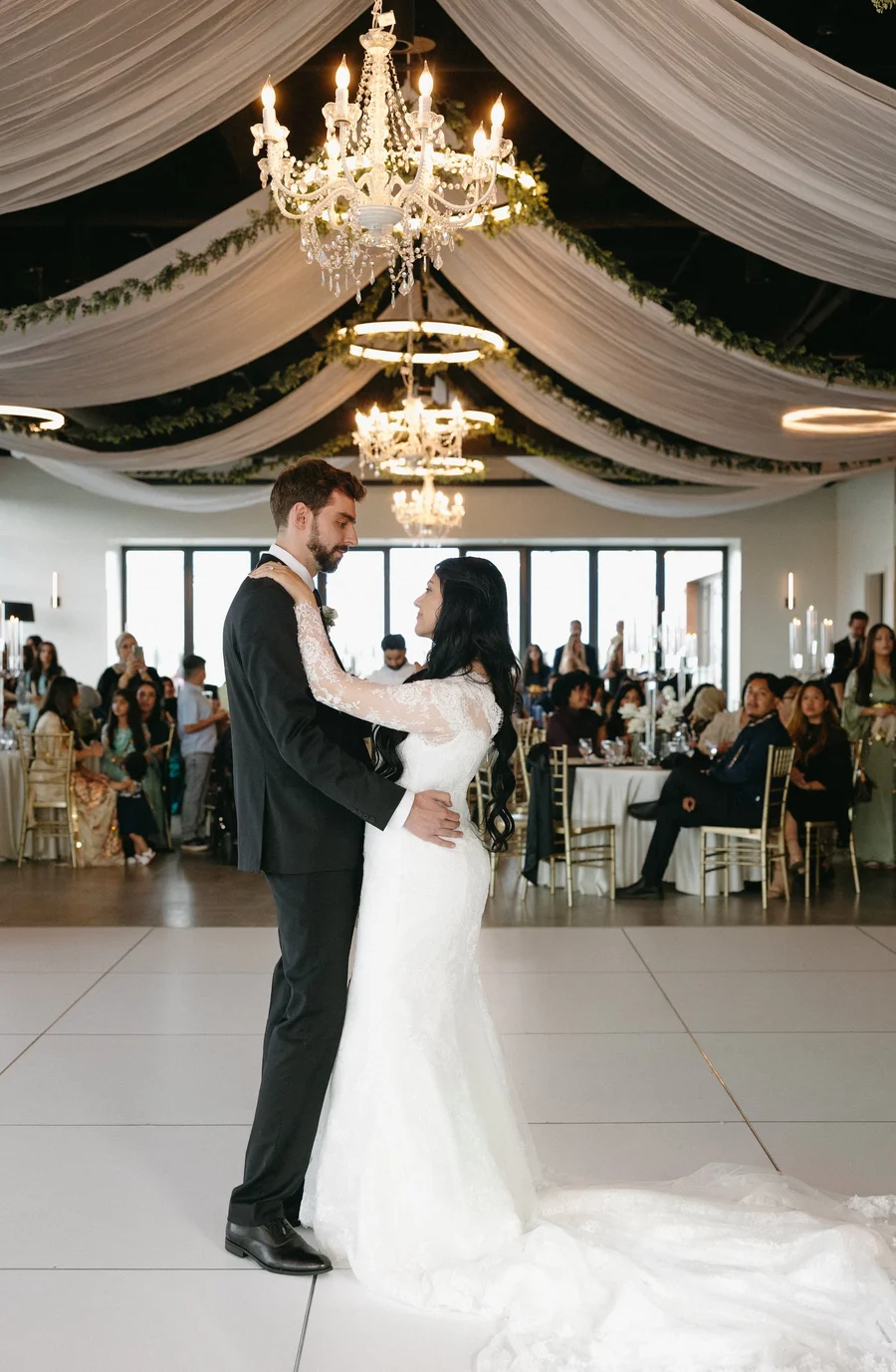 Bride and groom sharing a first dance beneath draped fabric and chandeliers