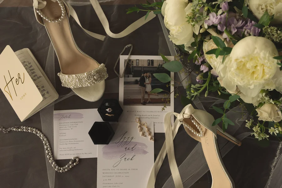 Wedding day details with heeled sandals, flowers and stationery in a flat lay
