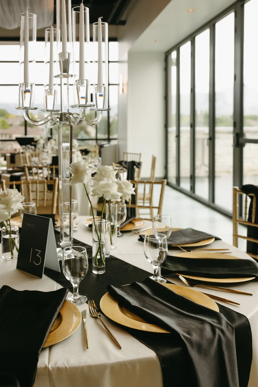Black and gold table setting with a tall candelabra and window views