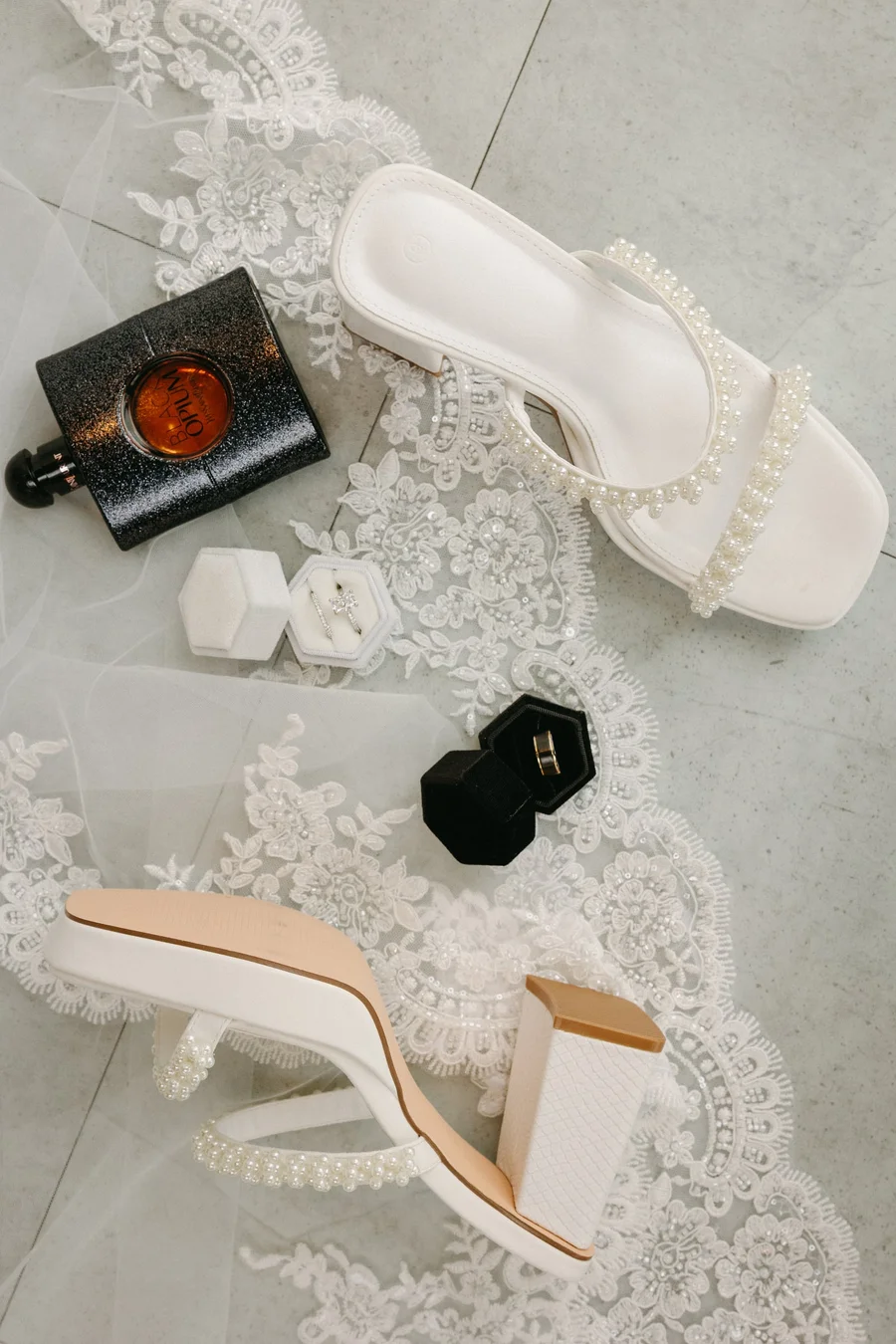 Wedding flat lay with white heeled sandals, perfume and a ring box on lace