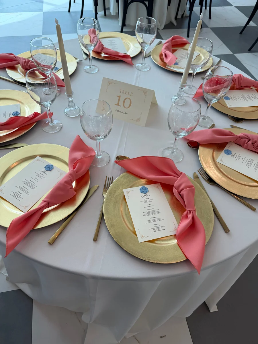 Table setting with gold chargers, coral napkins, menus and table number ten