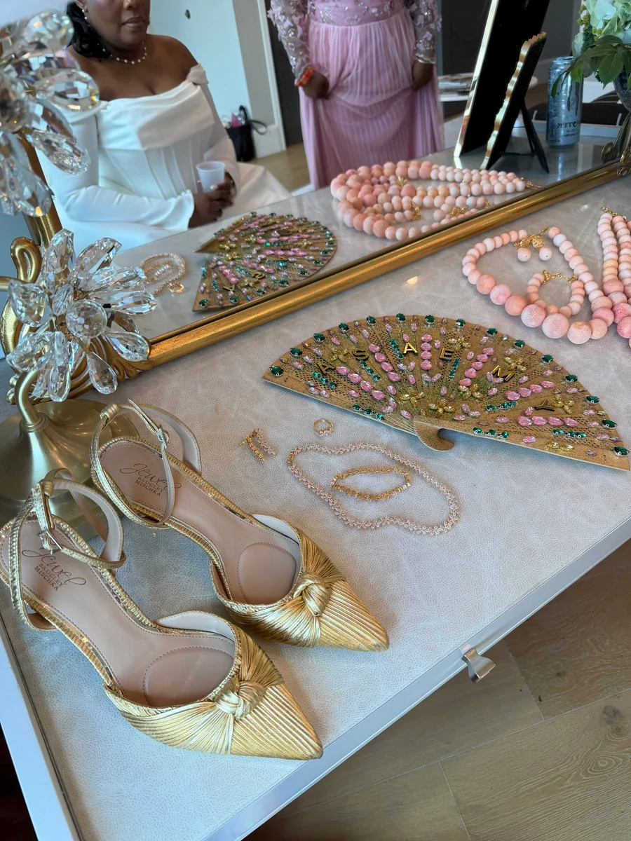 Gold heels, jewelry and a decorative fan displayed on a mirrored tray