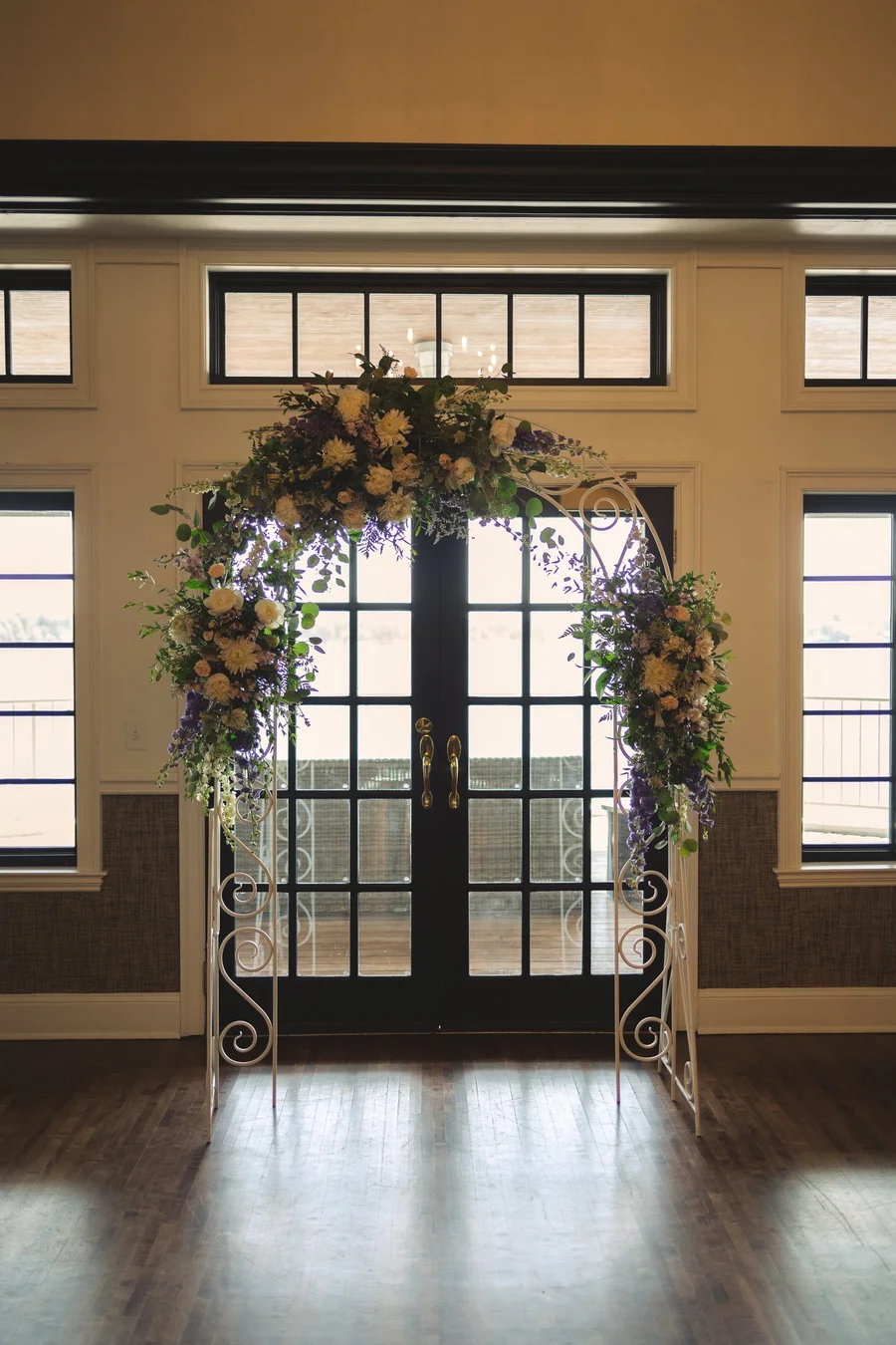 Floral arch in front of glass doors in a wood-paneled ceremony room