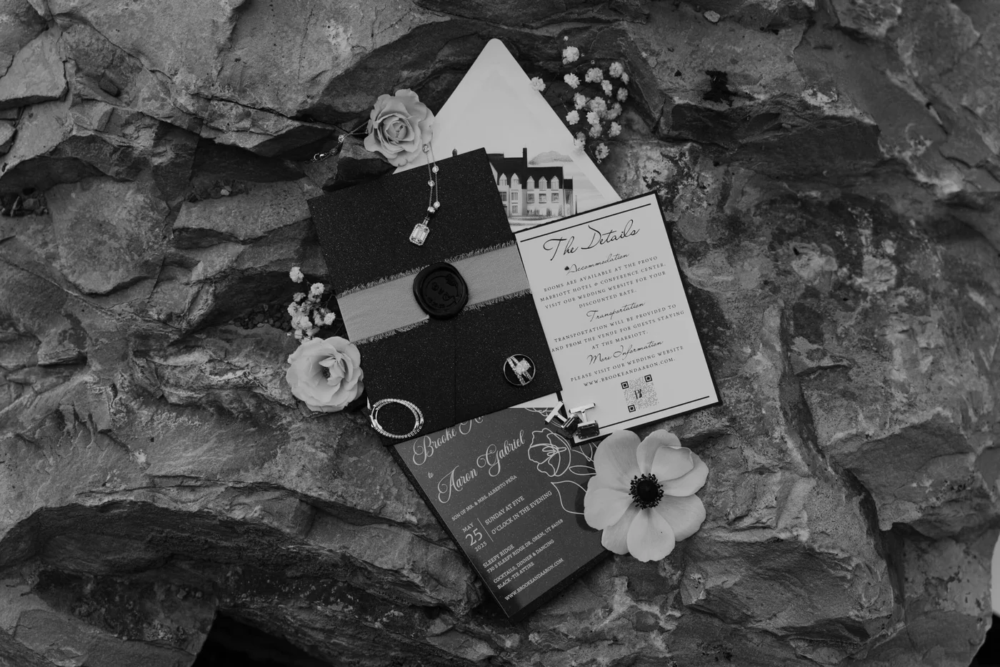 A wedding invitation suite, florals and details arranged on dark stone, in black and white.